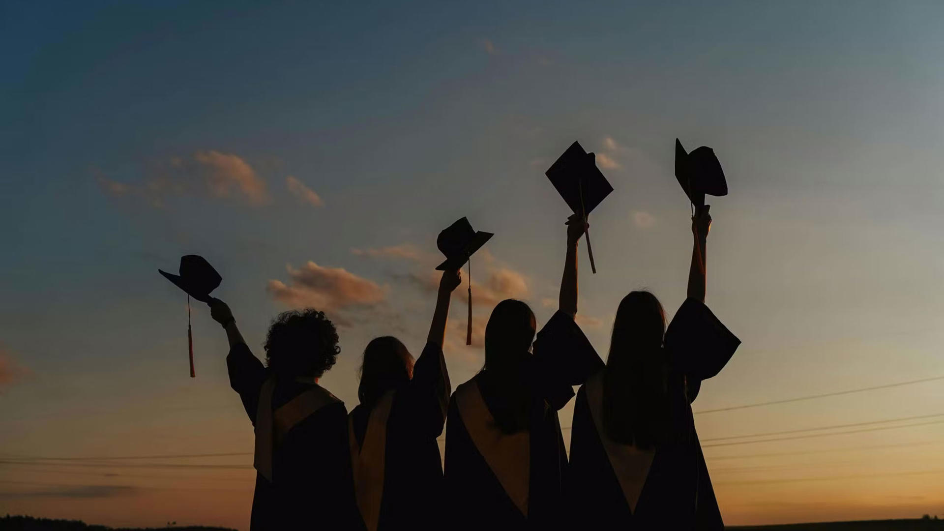 silhouette of 4 people graduating and lifting up their graduation caps